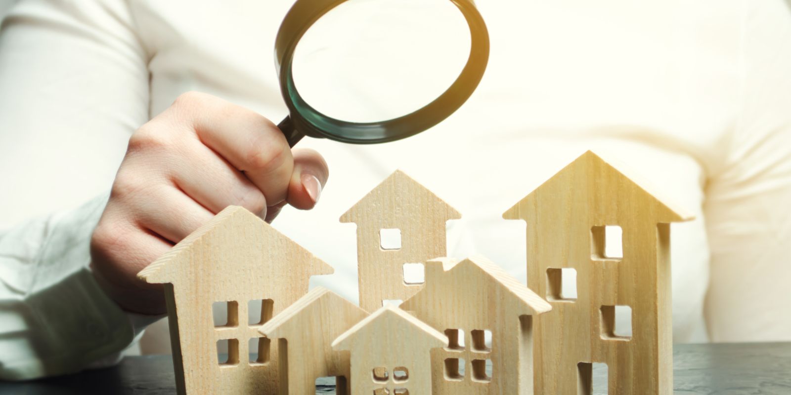 Person holding a magnifying glass above multiple wooden houses